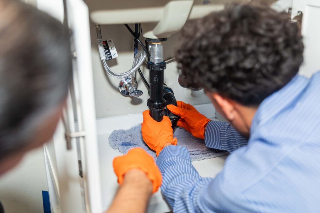 Two plumbers working under a sink to repair plumbing