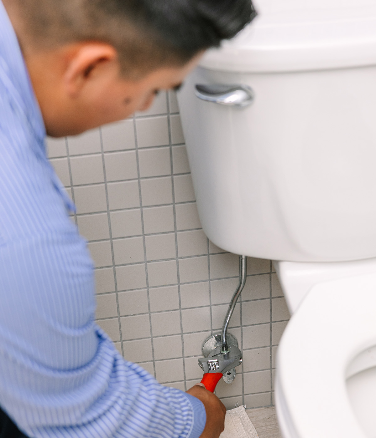 A plumber fixing a toilet with a wrench in a bathroom.