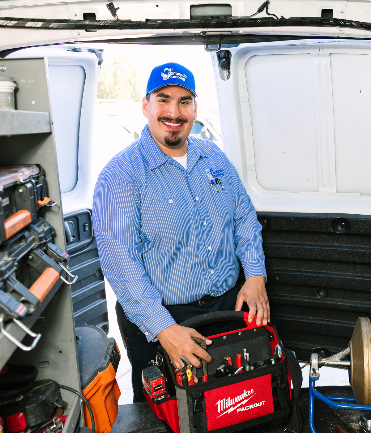 Al Coronado plumber holding a tool bag, standing inside his organized service van.